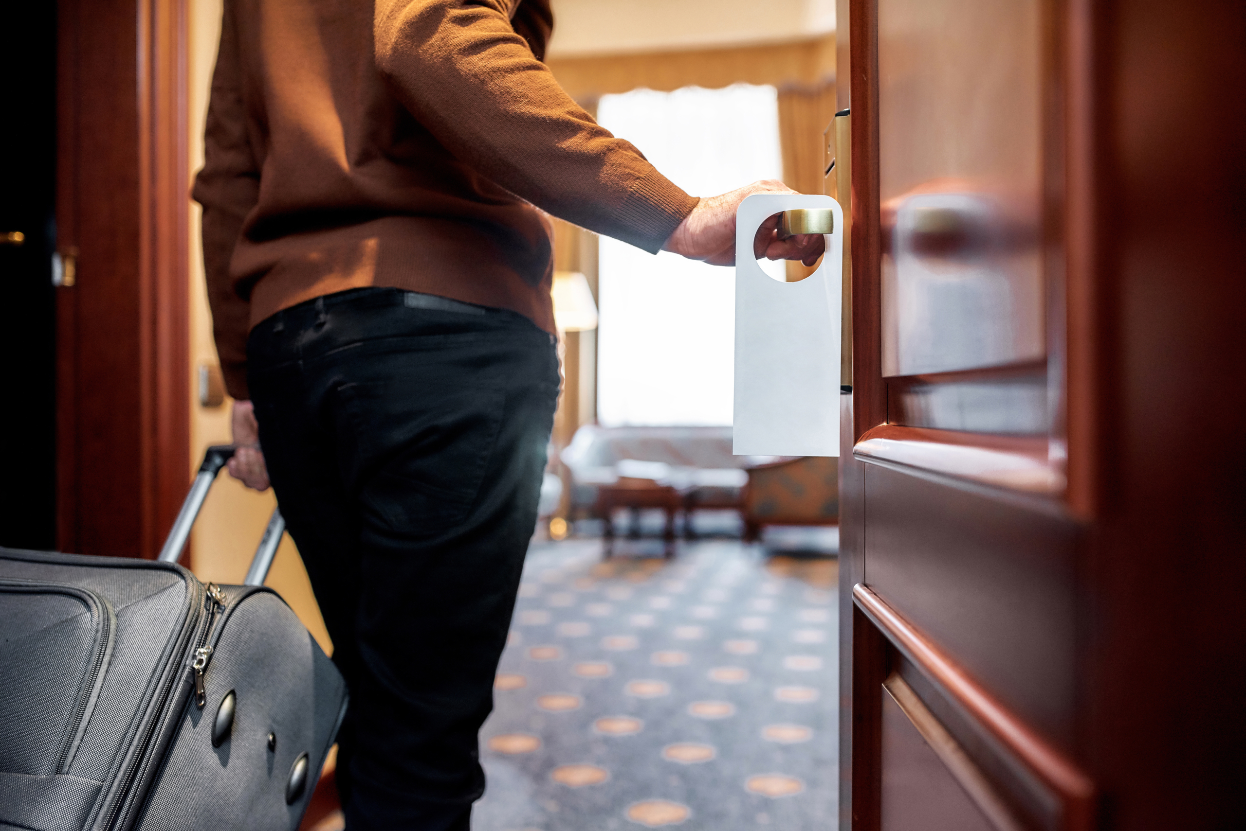 Cropped shot of middle-aged businessman in casual wear with suitcase entering his room. A door with a sign.